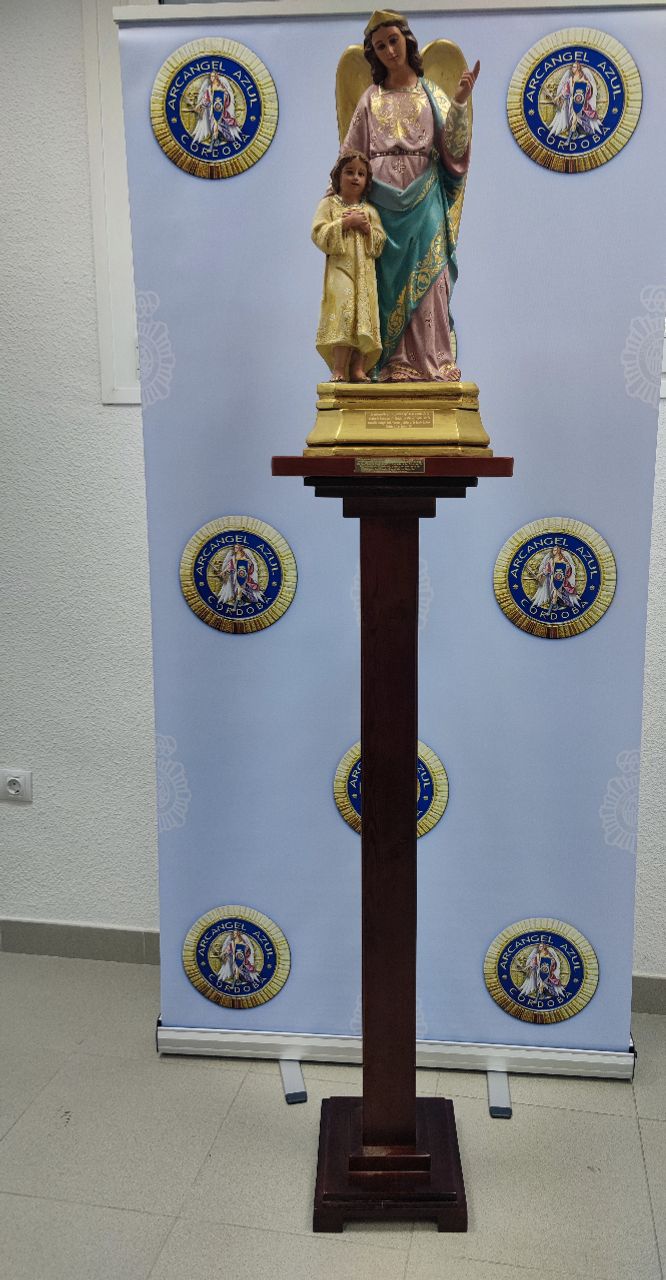 Según acuerdo por unanimidad de la Junta Directiva, en reunión ordinaria de 25 de mayo de 2021 y debidamente autorizados, por parte de un profesional carpintero se ha procedido a fabricar una peana de madera y que sustentará el Santo Ángel de la Guarda que hay en la Comisaría Provincial y que preside todos los actos institucionales. En la fotografía podéis ver el resultado de dicha restauración y como queda en la peana donada y sufragada por nuestra Asociación.