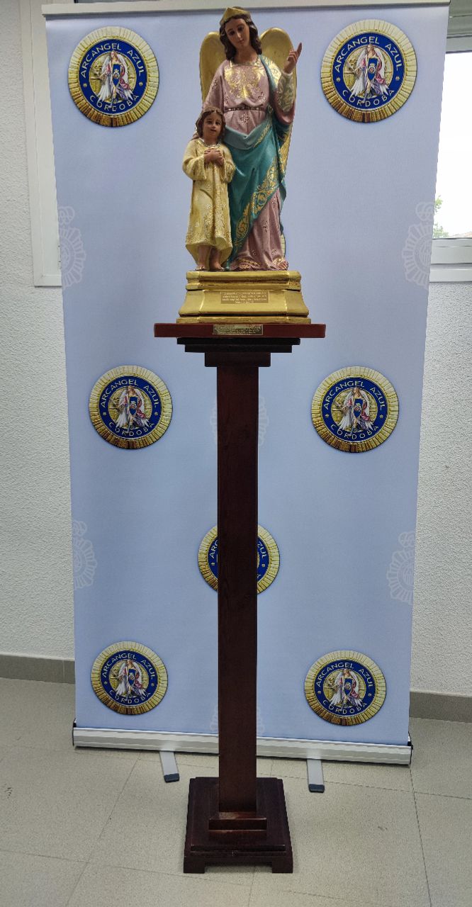 Según acuerdo por unanimidad de la Junta Directiva, en reunión ordinaria de 25 de mayo de 2021 y debidamente autorizados, por parte de un profesional carpintero se ha procedido a fabricar una peana de madera y que sustentará el Santo Ángel de la Guarda que hay en la Comisaría Provincial y que preside todos los actos institucionales. En la fotografía podéis ver el resultado de dicha restauración y como queda en la peana donada y sufragada por nuestra Asociación.